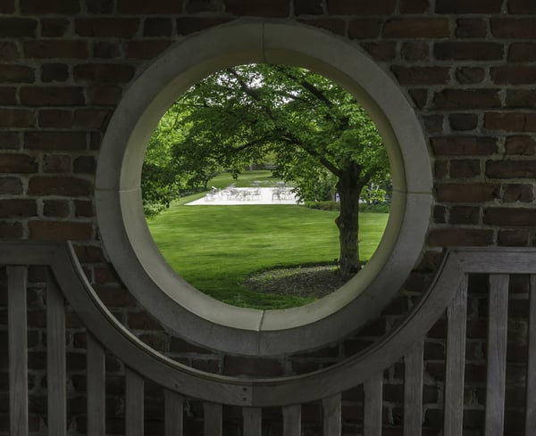Outside world at a glance Four-part porthole in a walled garden with a view of spacious green lawn, trees, and patio across the way